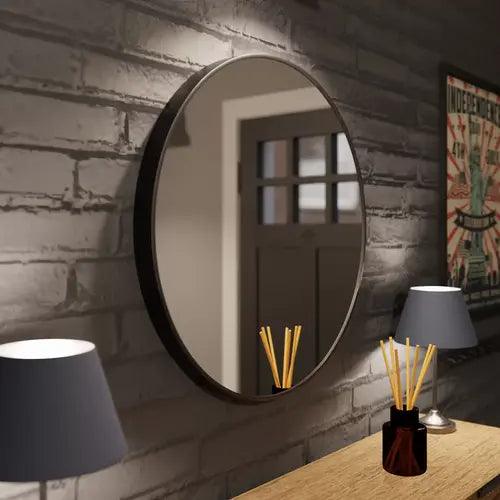 Miroir rond noir de 60 cm placé au-dessus d'une console en bois, entouré de lampes et de décoration murale