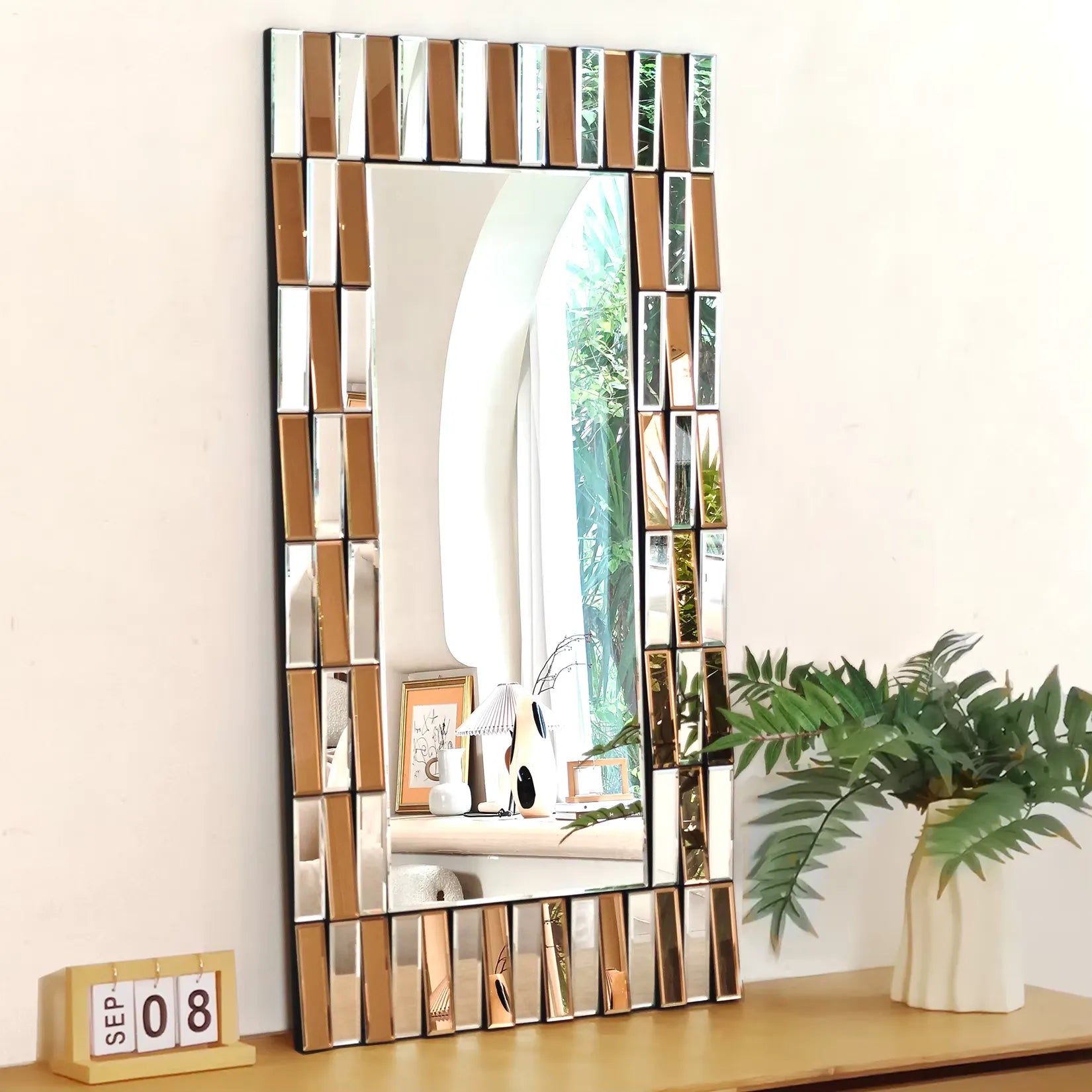 Miroir doré design rectangulaire captant la lumière naturelle sur un meuble bois clair.